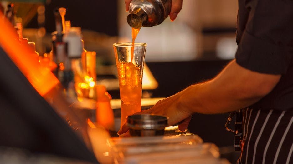 Barman préparant un cocktail devant un arrière-bar réfrigéré professionnel